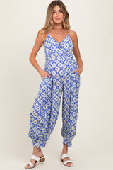 woman wearing a blue floral maternity jumpsuit with a v-neckline and pockets, styled with white sandals