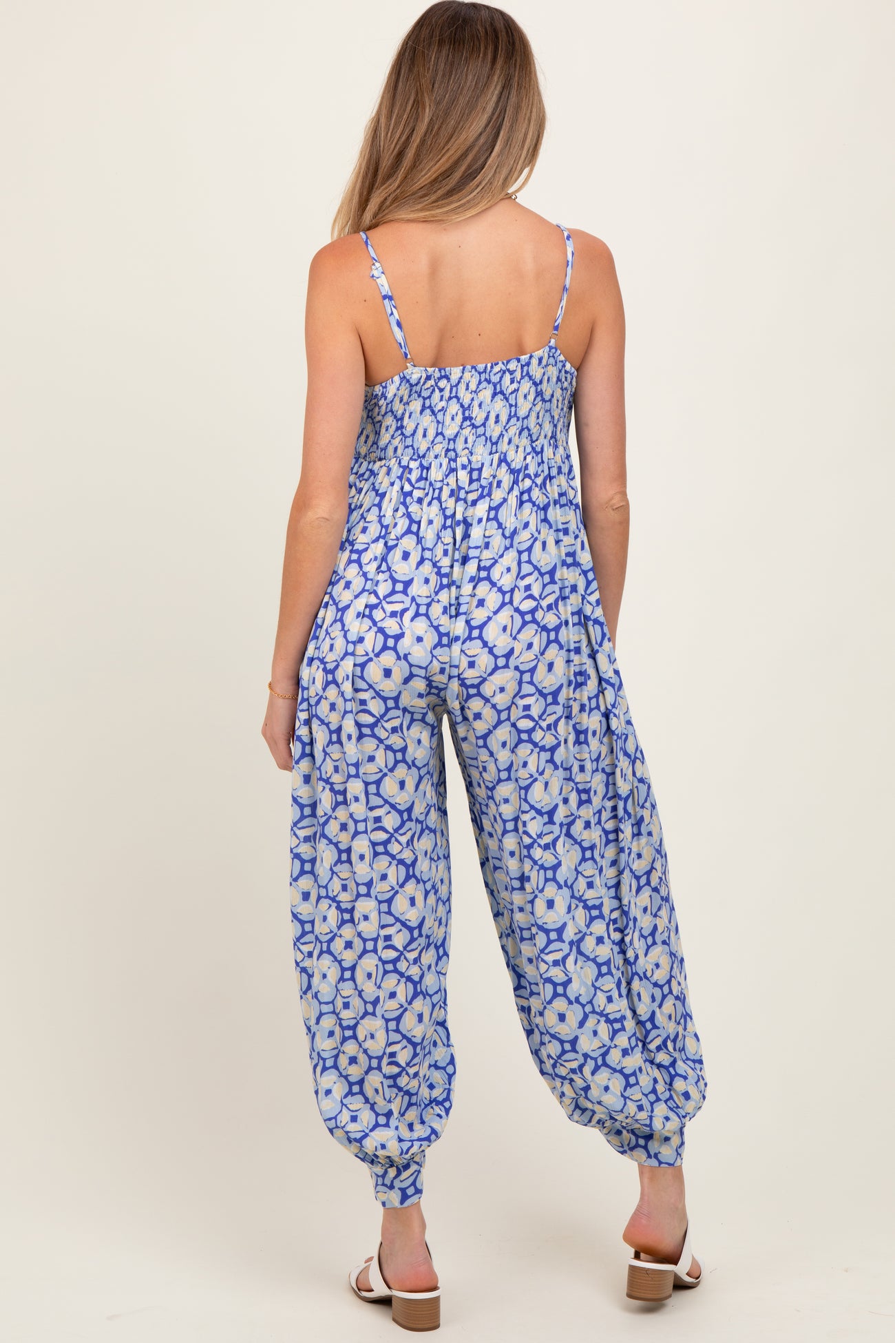 woman wearing a blue floral maternity jumpsuit with a smocked back and harem-style pant legs