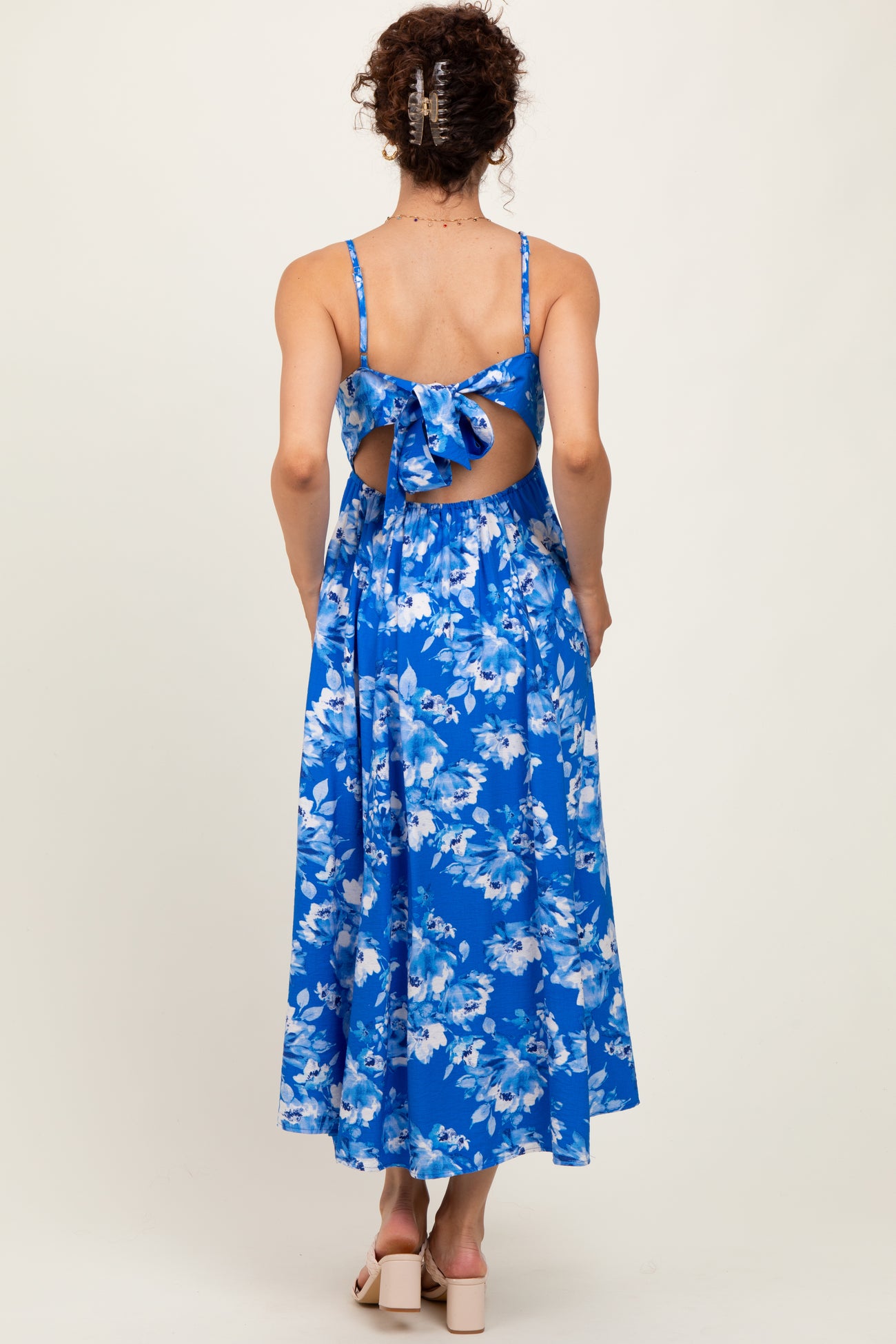 woman wearing a blue floral midi dress with a back tie detail and open back, showing a flowy skirt