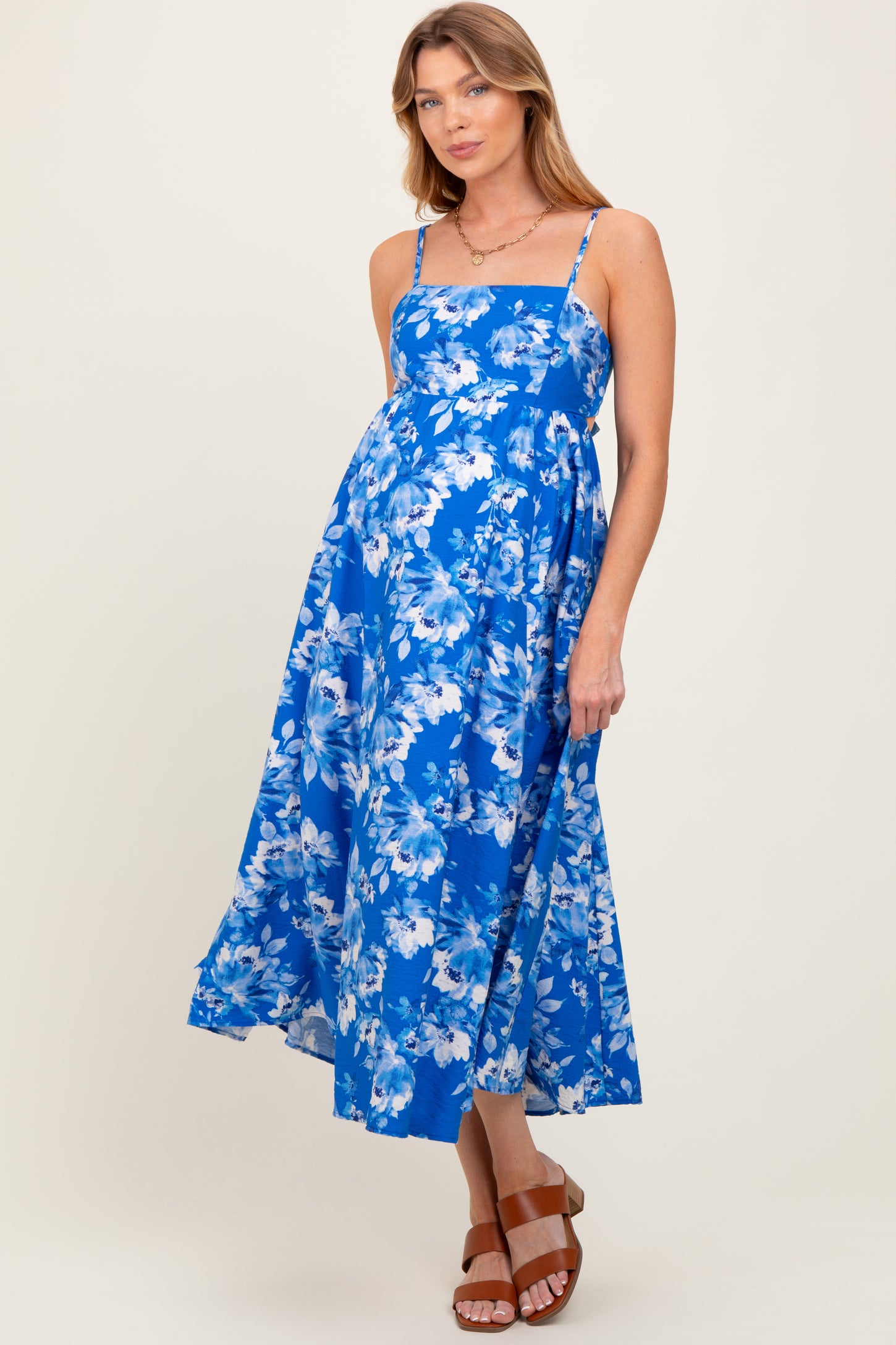 woman wearing a blue floral maternity dress with a fitted bodice and flowing skirt, displaying a baby bump