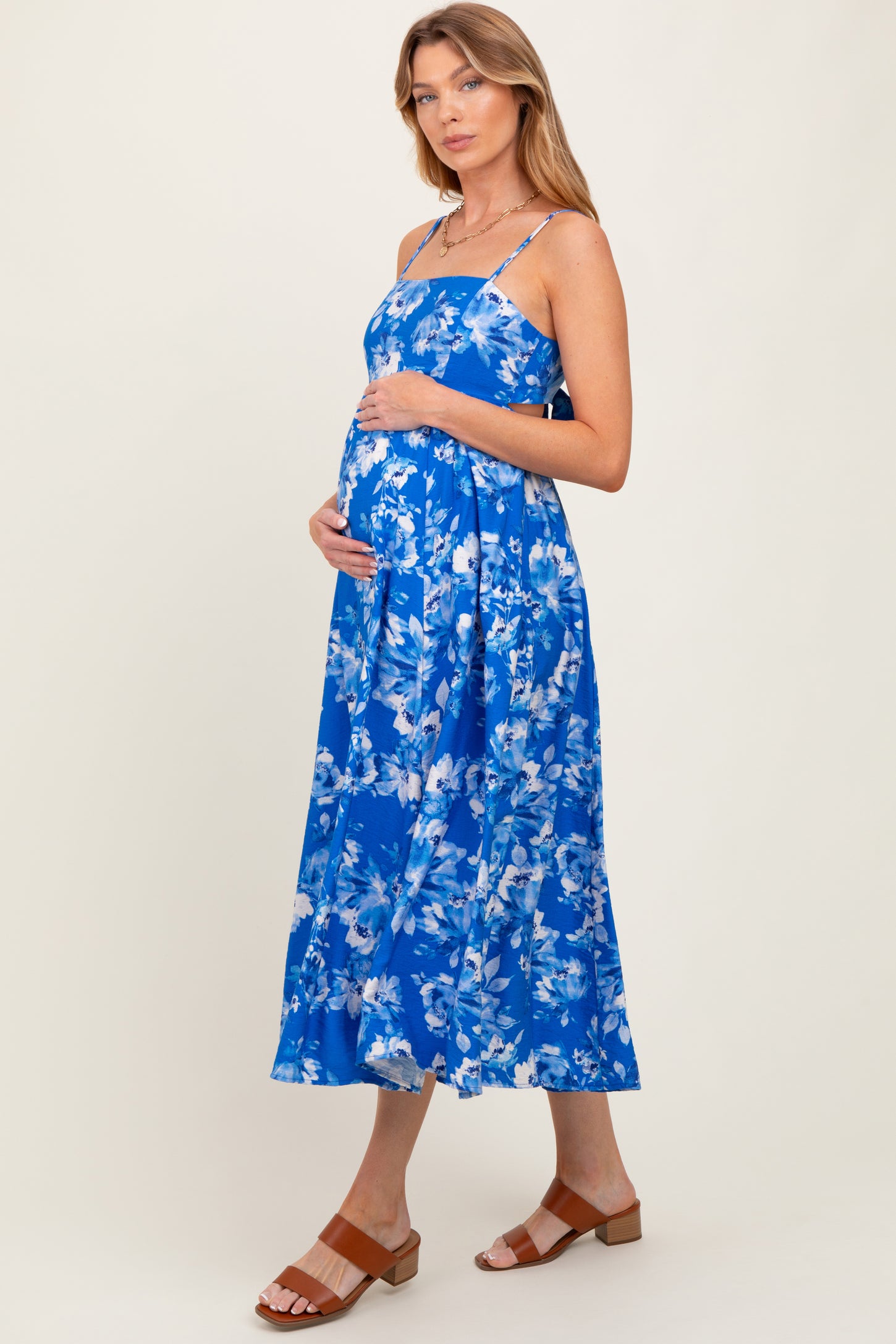 woman wearing a blue floral maternity dress, showcasing her baby bump, with spaghetti straps and a flowing skirt
