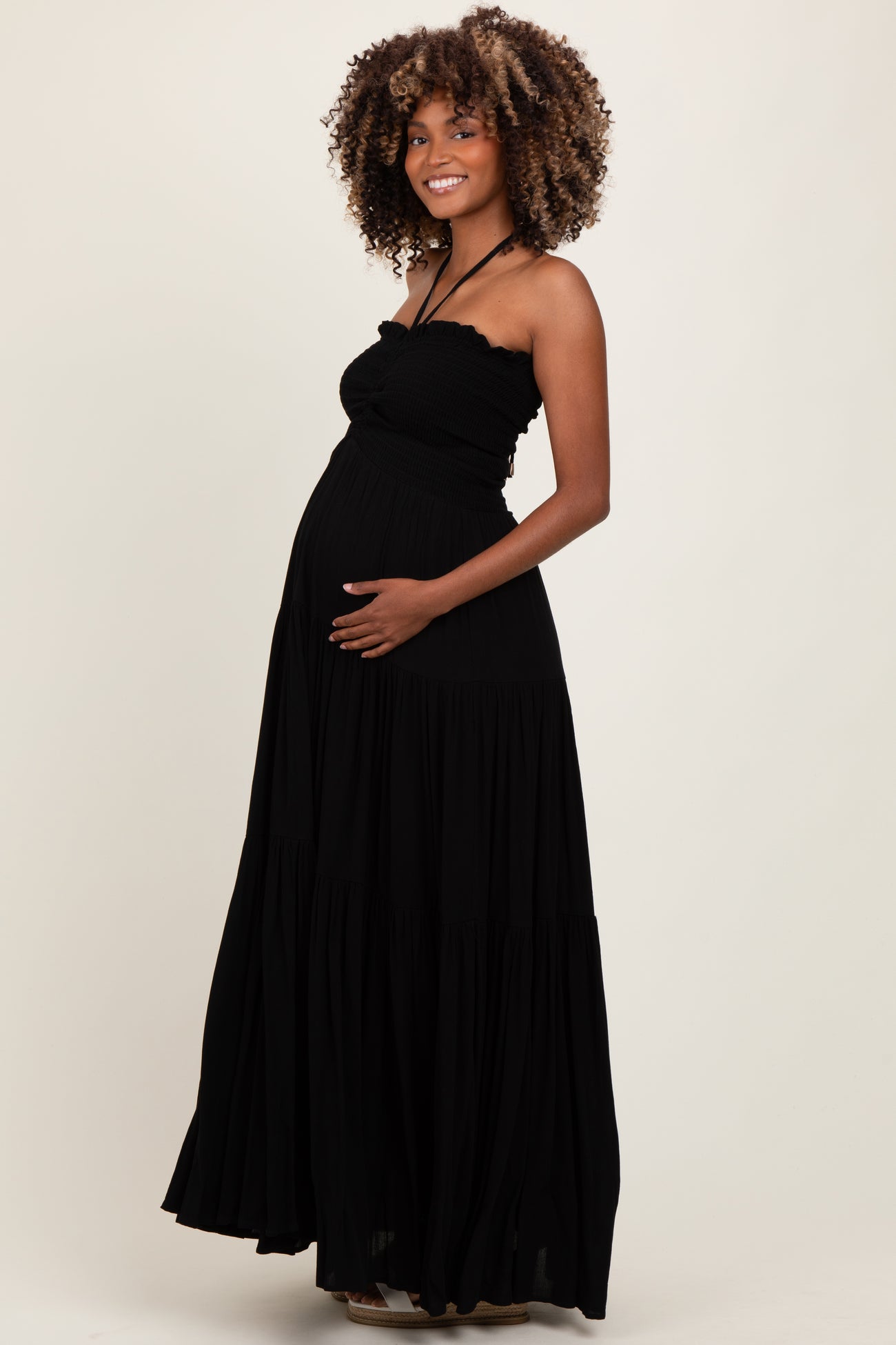 woman wearing a black maternity maxi dress with a fitted bodice and tiered skirt, showing her baby bump