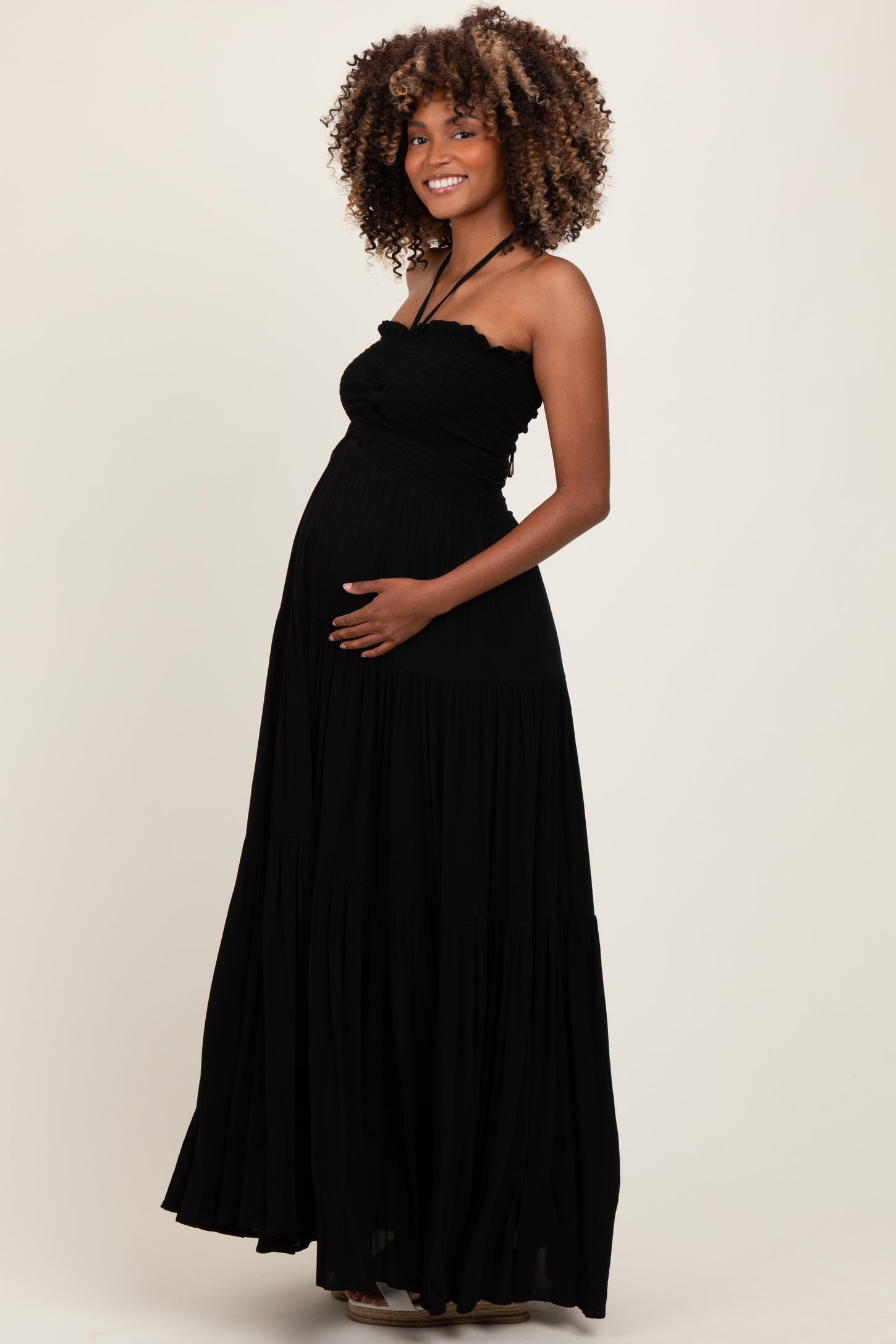 woman wearing a black maternity maxi dress with a fitted bodice and tiered skirt, showing her baby bump