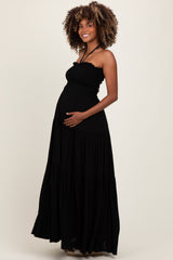 woman wearing a black maternity maxi dress with a fitted bodice and tiered skirt, showing her baby bump