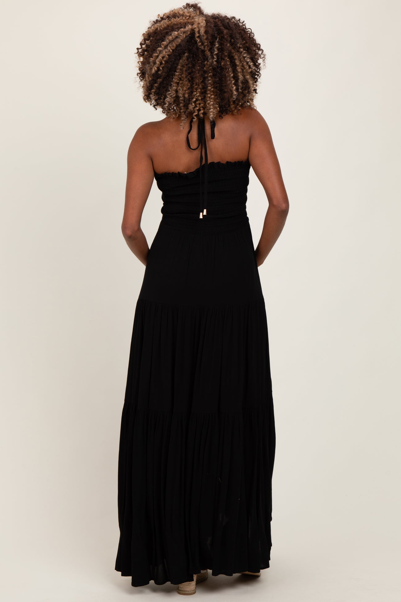 woman wearing a black strapless maxi maternity dress with a fitted bodice and tiered skirt from the back