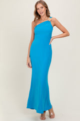 woman wearing a bright blue one-shoulder maxi dress with a decorative brooch detail and posing confidently