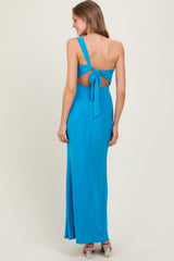 woman wearing a vibrant blue one-shoulder dress with a cut-out back and tie detail, standing against a neutral background