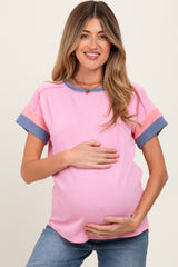 woman wearing a pink ribbed maternity top with blue striped sleeves and holding her baby bump