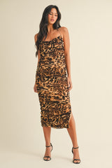 woman wearing a brown leopard print midi dress with ruching and a side slit, standing in strappy black heels