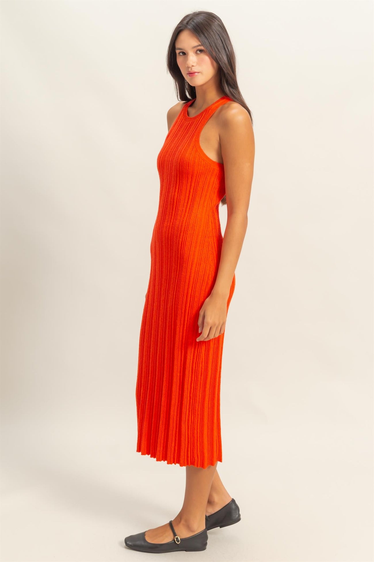 woman wearing a fitted orange ribbed midi dress with a sleeveless design and side cutouts, standing sideways
