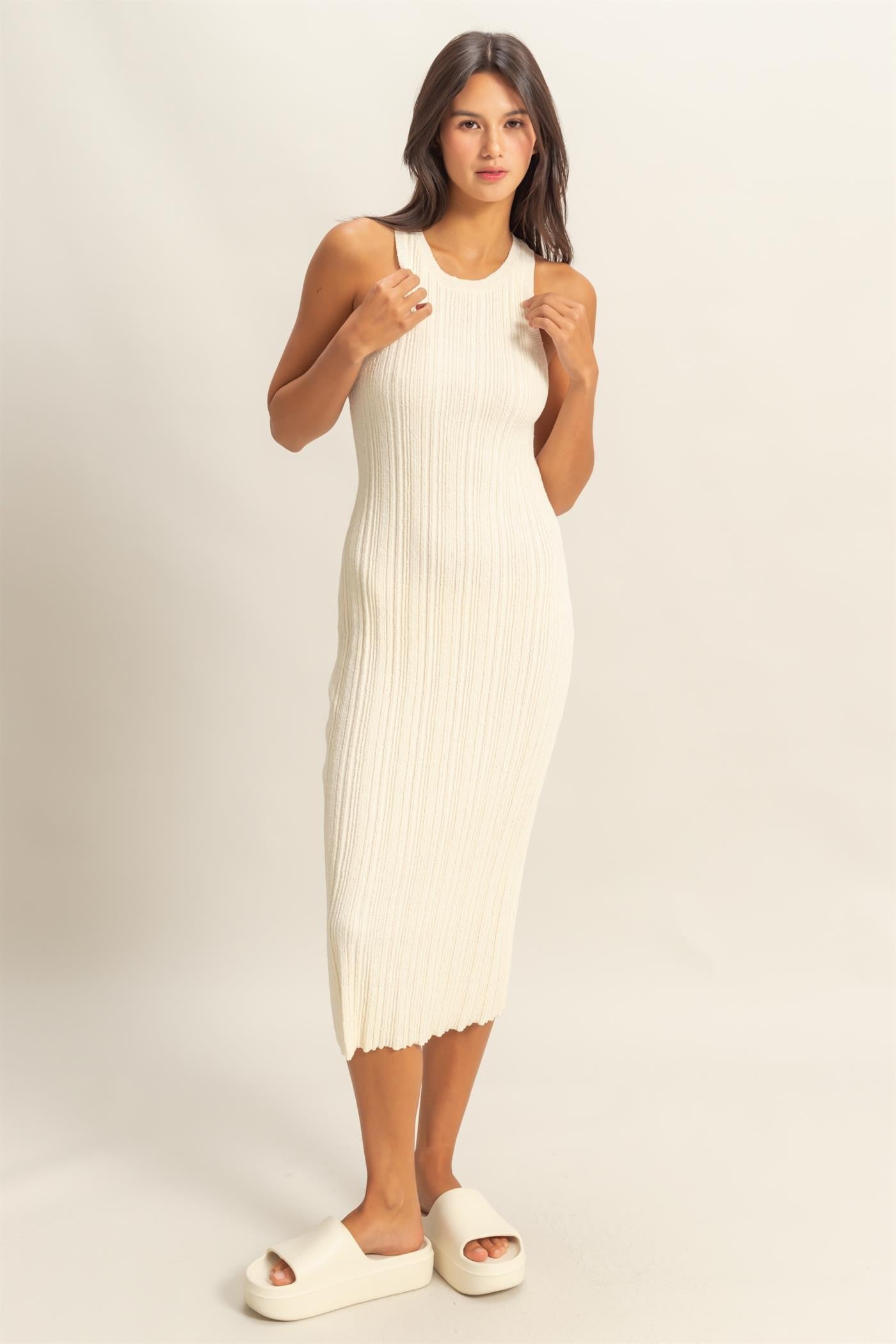 woman wearing a cream ribbed knit midi dress with a scoop neckline and side slits, paired with white slide sandals