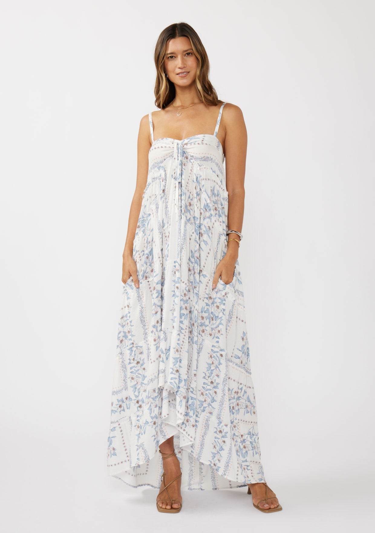 woman wearing a blue and white floral maxi dress with a hi-low hem and adjustable spaghetti straps