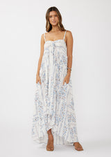 woman wearing a blue and white floral maxi dress with a hi-low hem and adjustable spaghetti straps