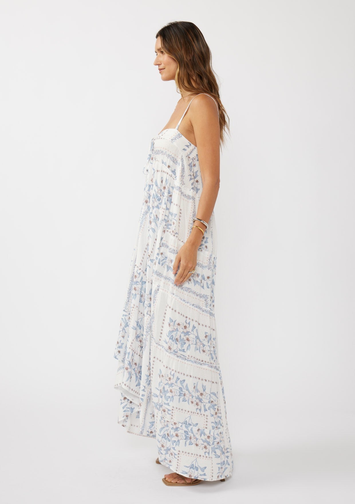 woman wearing a white and blue floral maxi dress with adjustable straps and a flowy silhouette