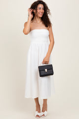 woman wearing a white strapless midi dress with a fitted bodice and flowy skirt, holding a black handbag