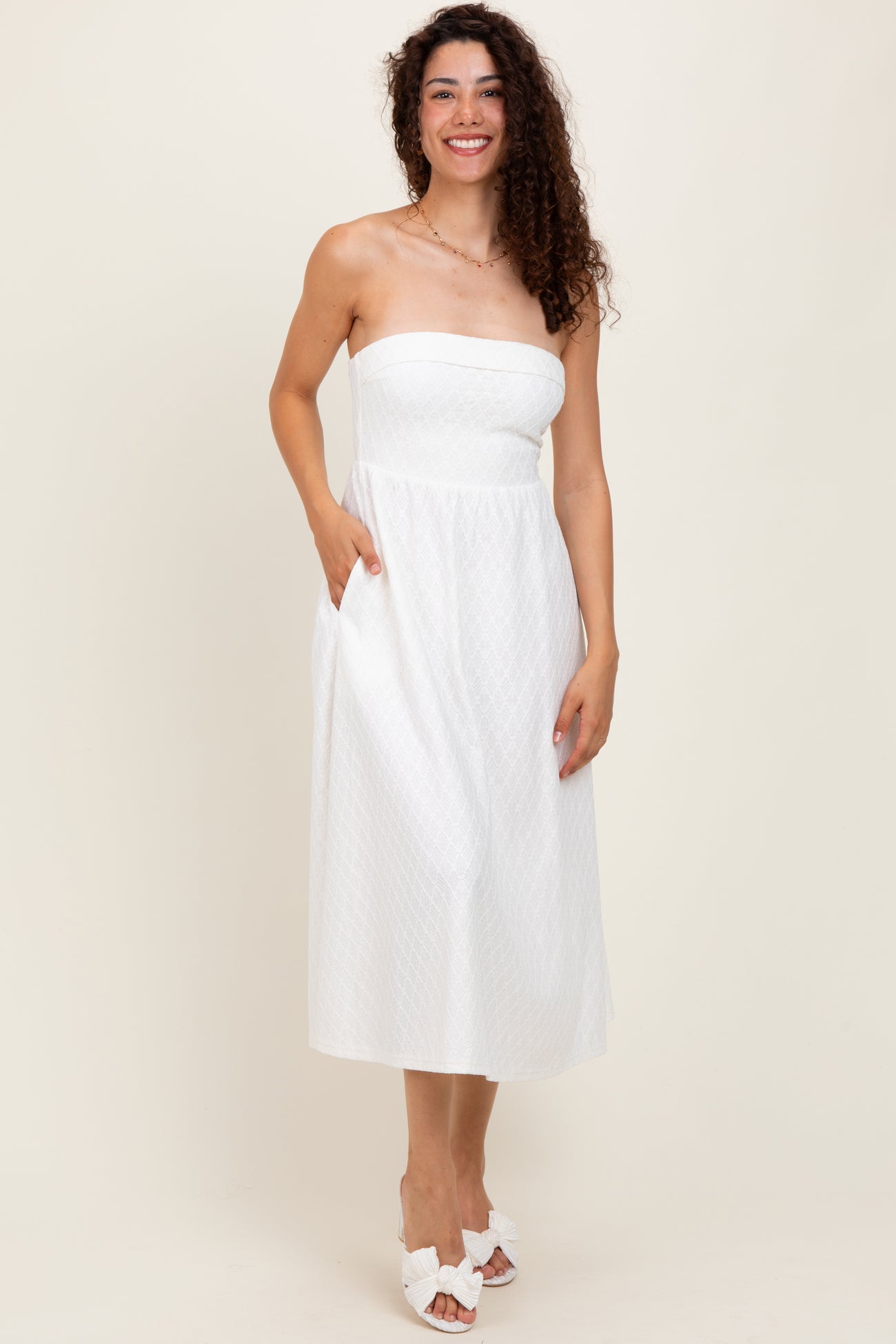 woman wearing a white strapless midi dress with a textured pattern and side pockets, standing on a neutral background