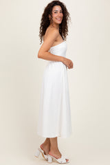 woman wearing a white strapless midi dress with a textured pattern and curly hair, standing sideways