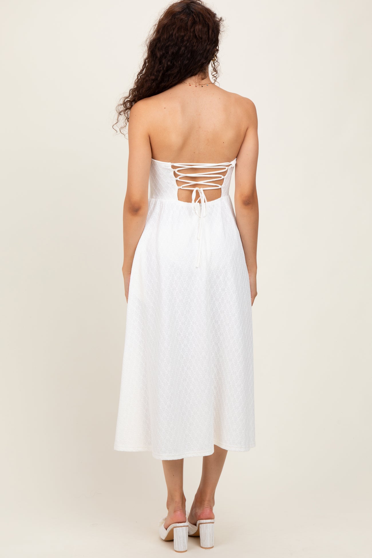 woman wearing a white strapless midi dress with a lace-up back and a flowy silhouette
