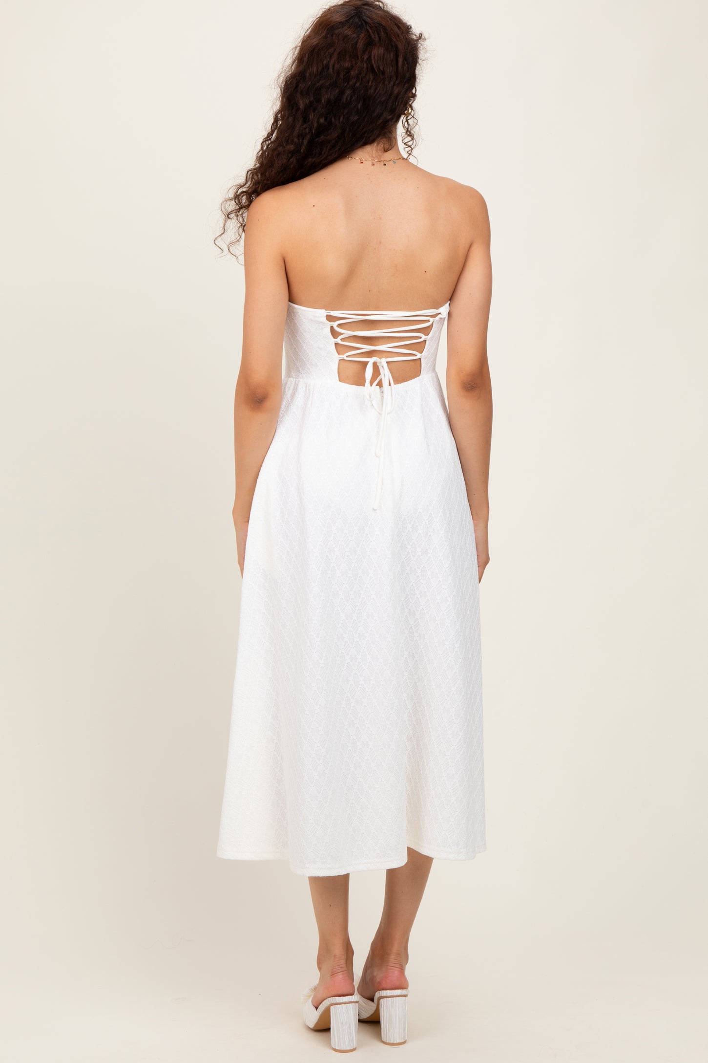 woman wearing a white strapless midi dress with a lace-up back and a flowy silhouette