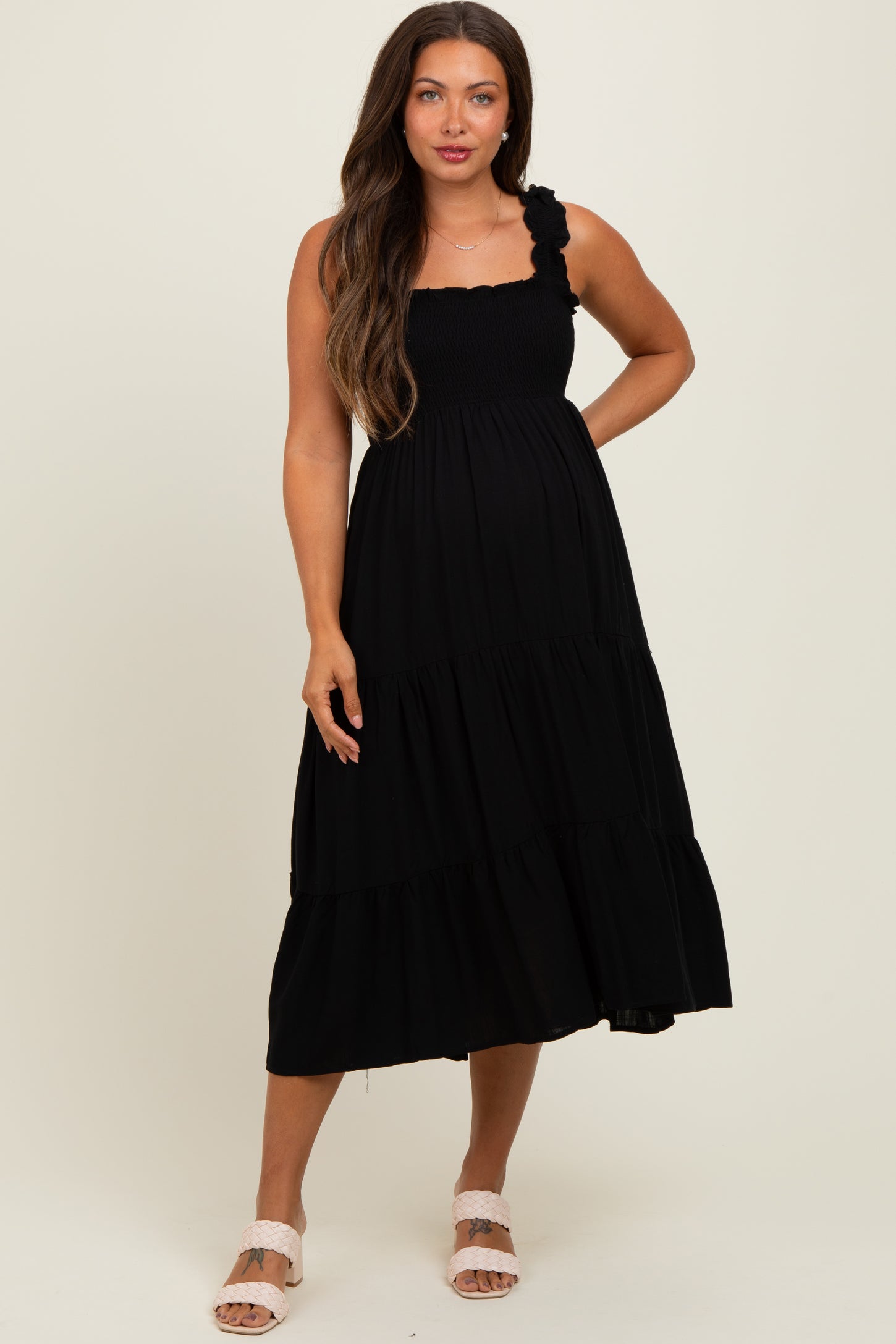 woman wearing a black smocked maternity dress with ruffled straps and tiered skirt