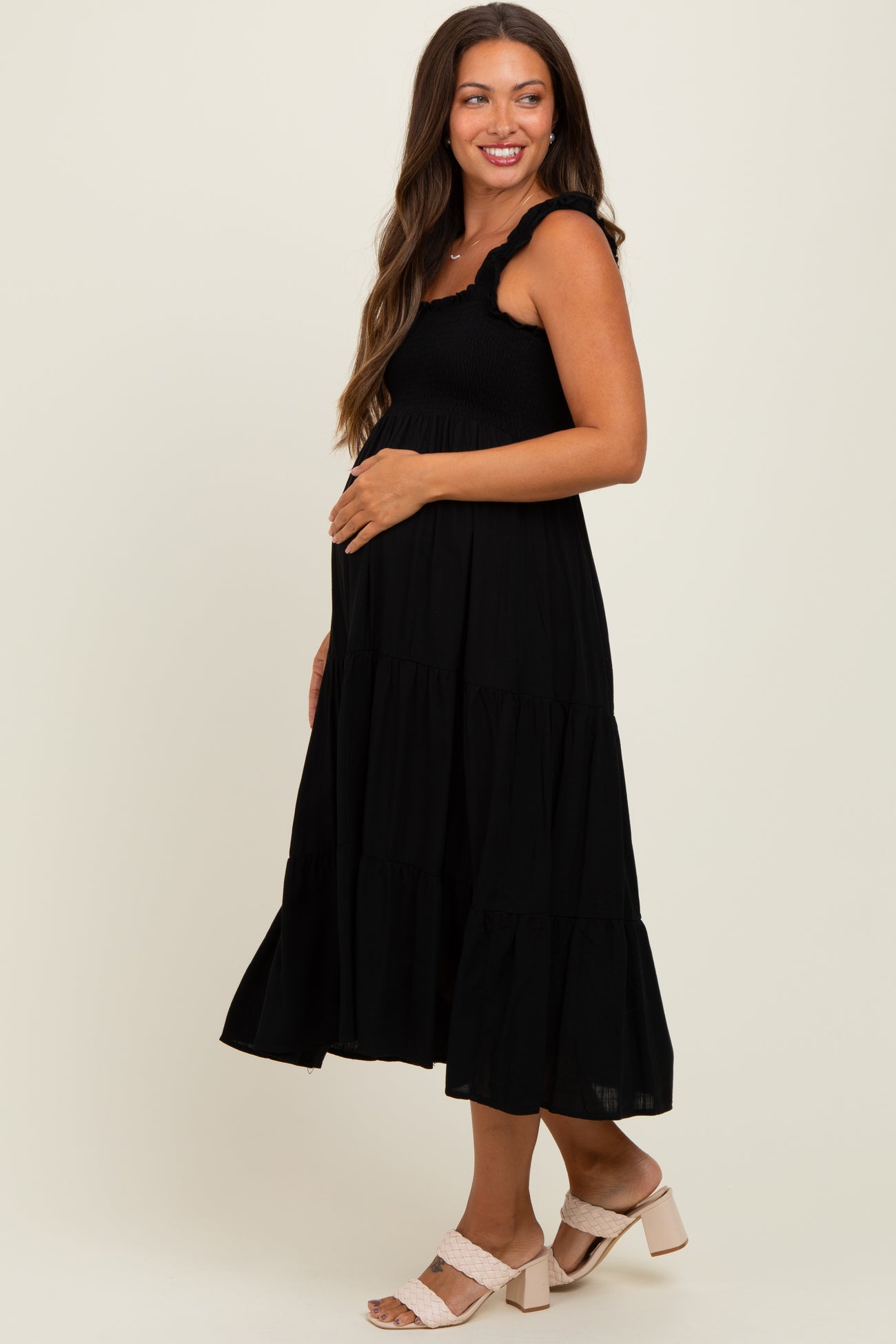 woman wearing a black maternity tiered maxi dress and gently holding her baby bump