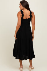 woman wearing a black maternity dress with ruffled straps and a tiered skirt, showing the back view