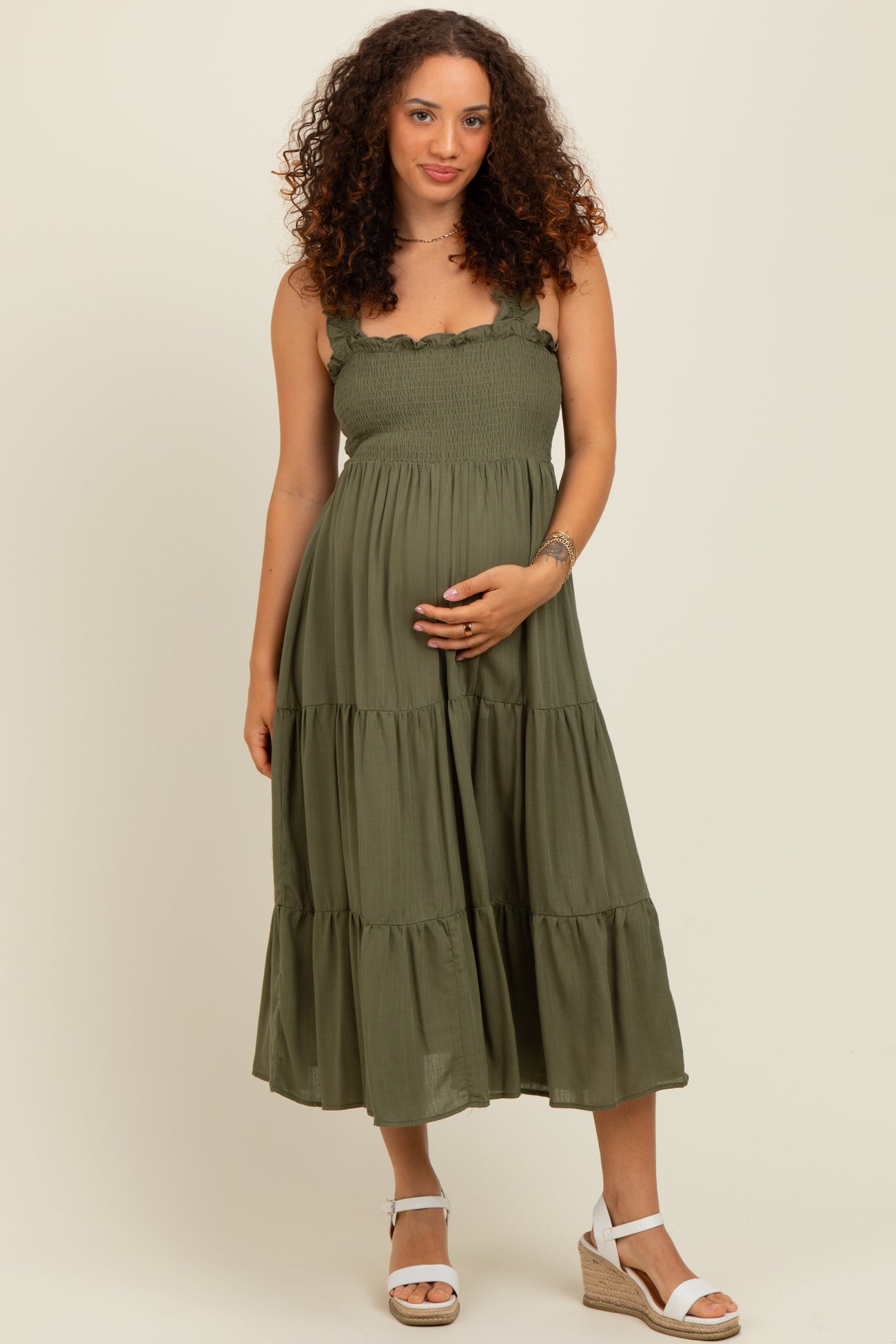 woman wearing a green maternity dress with ruffled straps and a tiered skirt, showing her baby bump