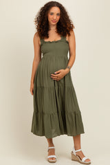 woman wearing a green maternity dress with ruffled straps and a tiered skirt, showing her baby bump