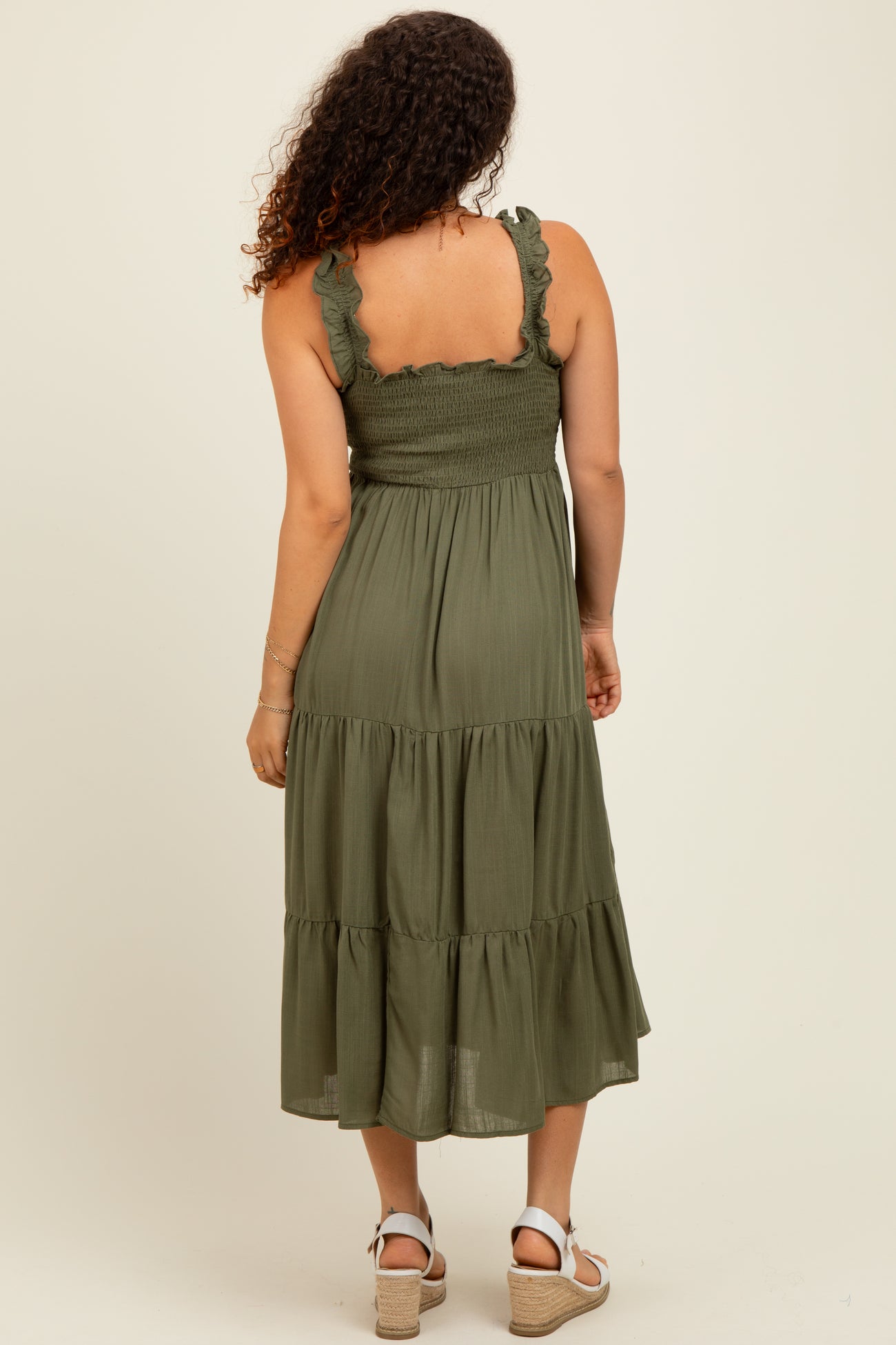 woman wearing an olive green maternity dress with ruffled straps and tiered skirt, showing her baby bump from behind