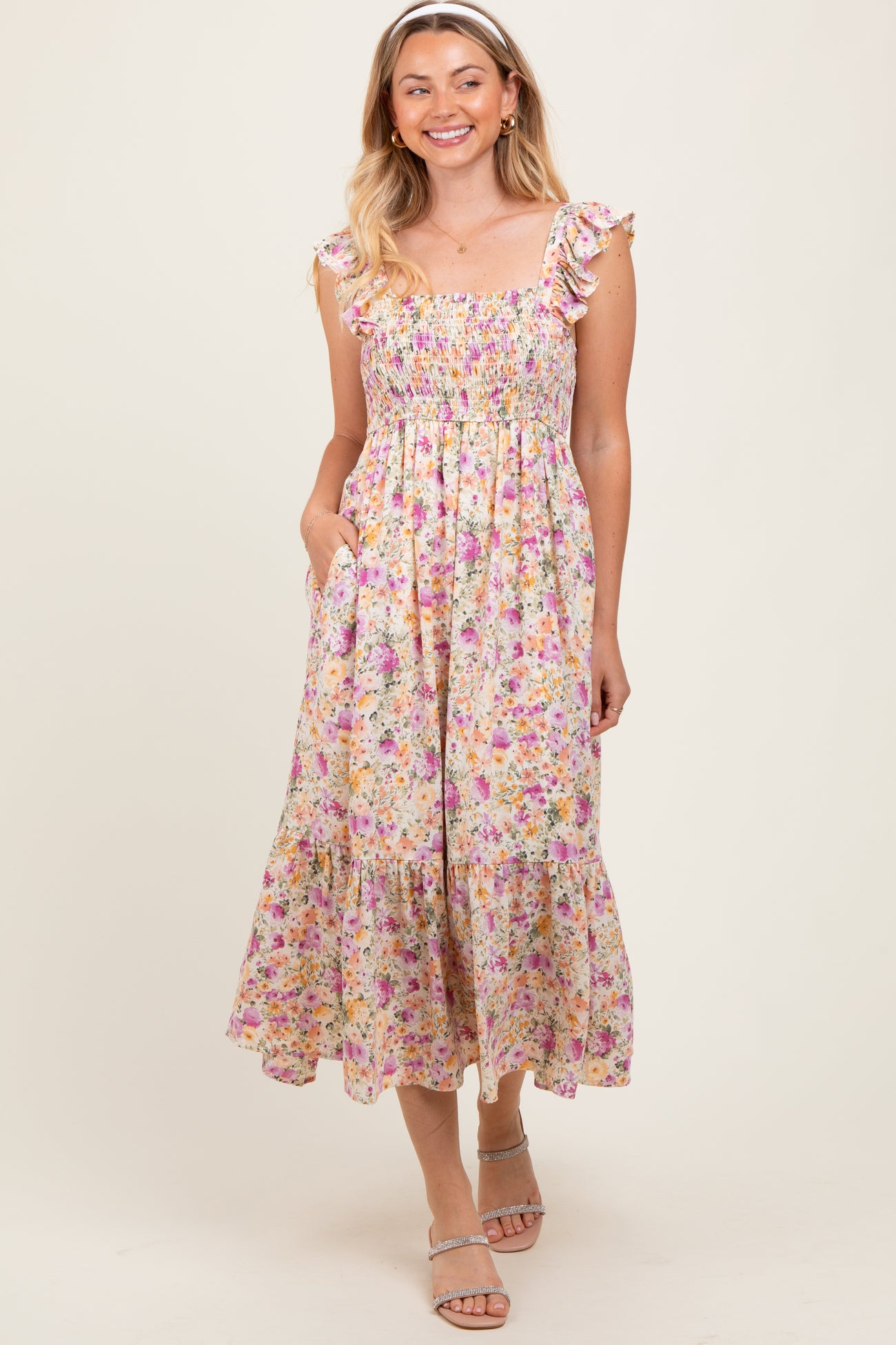 woman wearing a floral smocked midi dress with ruffle straps and pockets, standing and smiling