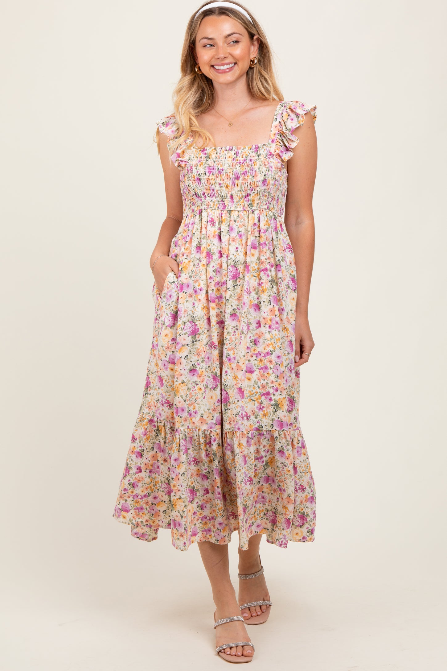 woman wearing a floral smocked midi dress with ruffle straps and pockets, standing and smiling