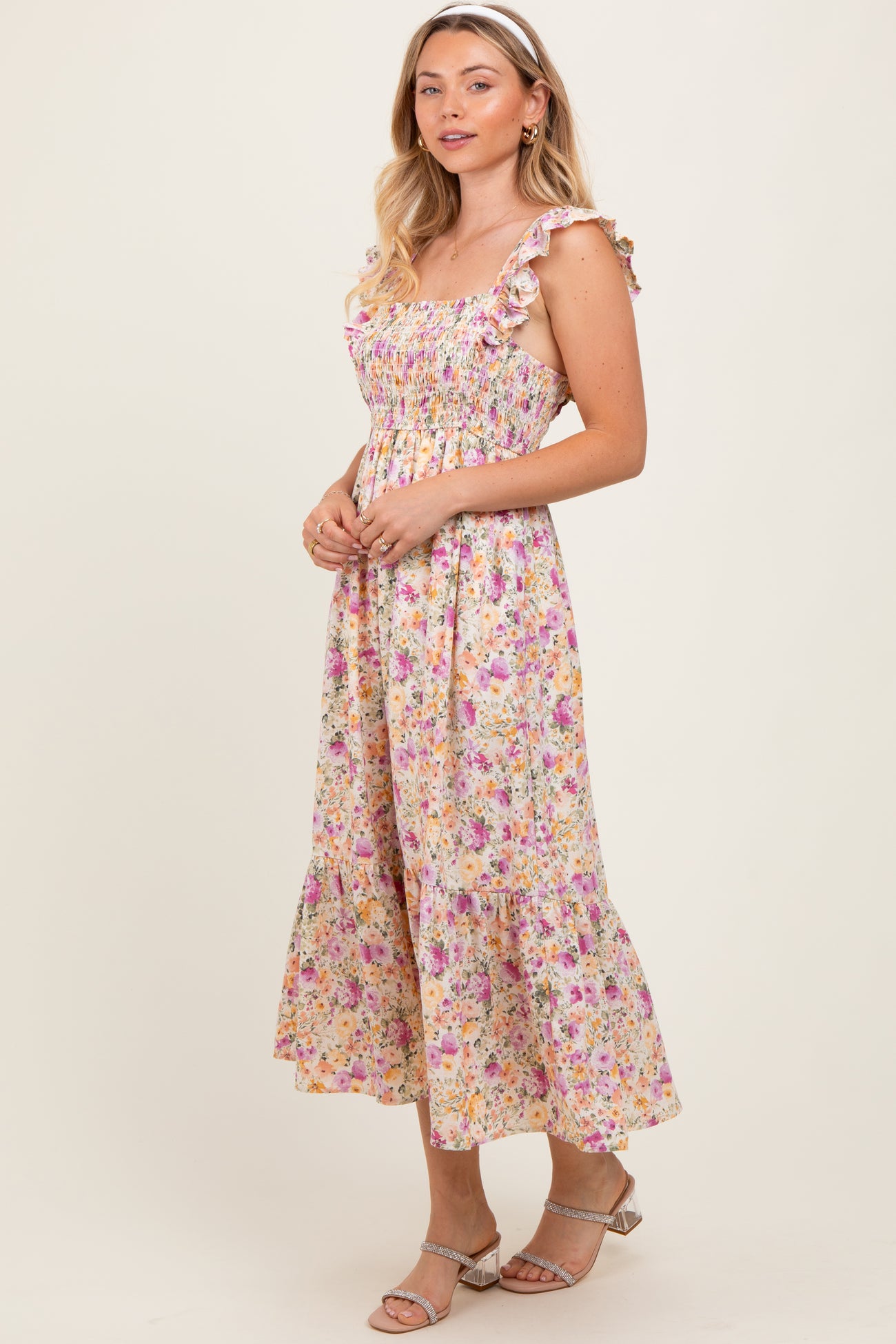 woman wearing a floral midi dress with ruffled straps and a fitted bodice, standing against a plain background