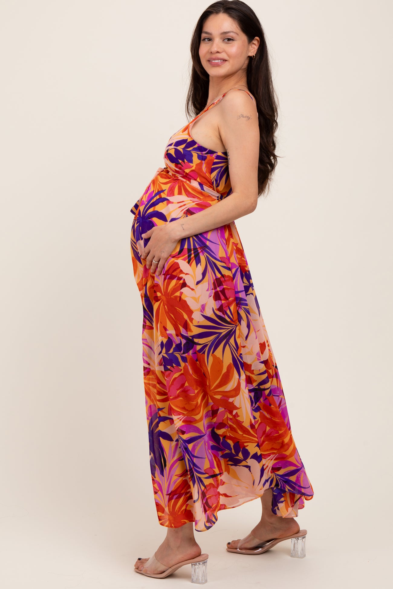 woman wearing a vibrant floral maxi maternity dress, showing her baby bump with a side pose