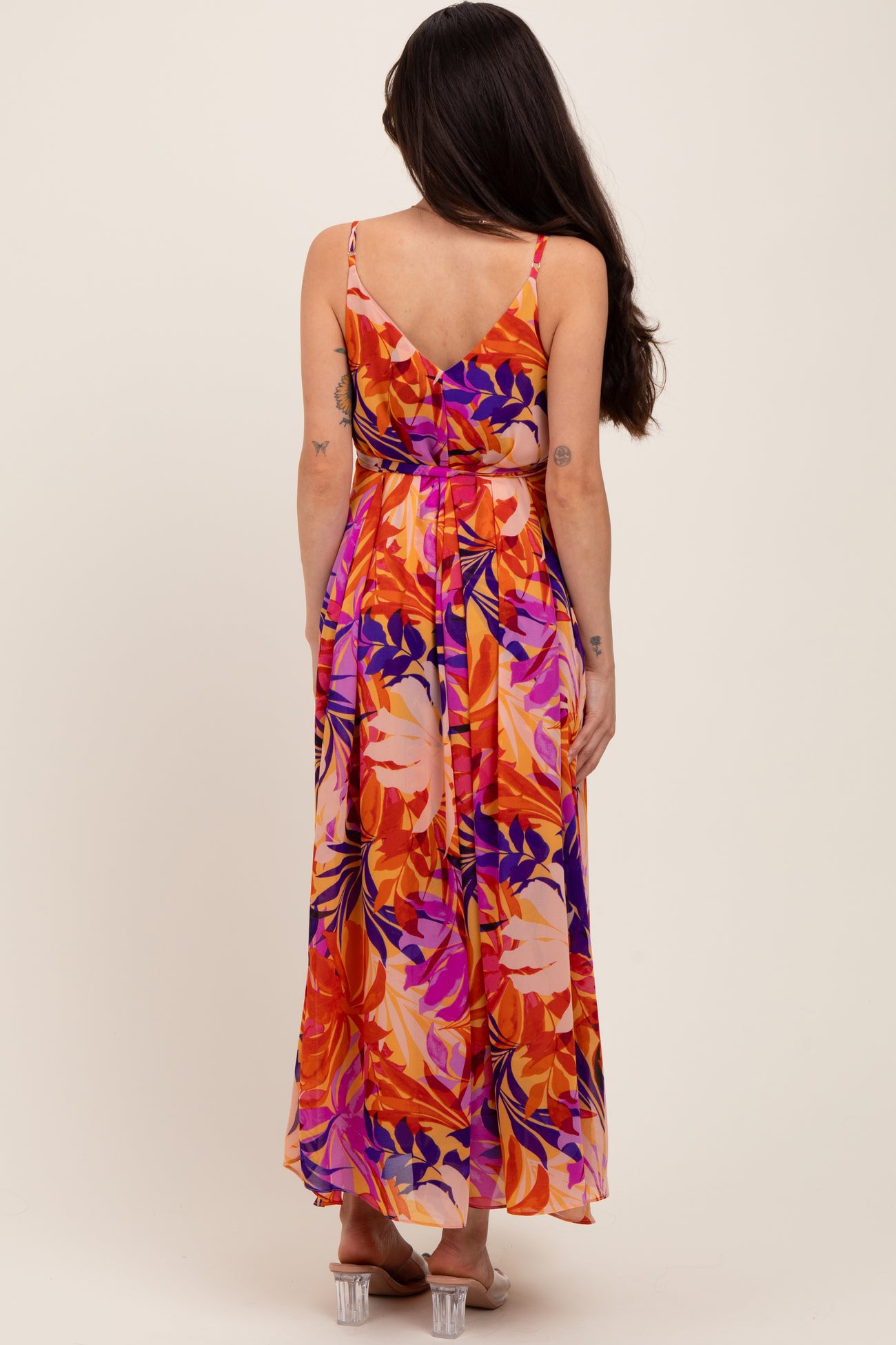 woman wearing a floral maxi maternity dress with a tieback in vibrant orange and purple hues