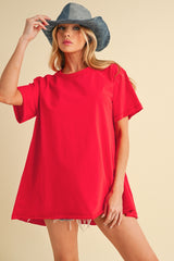 woman wearing a bright red oversized t-shirt with rolled sleeves and distressed denim shorts, accessorized with a blue hat