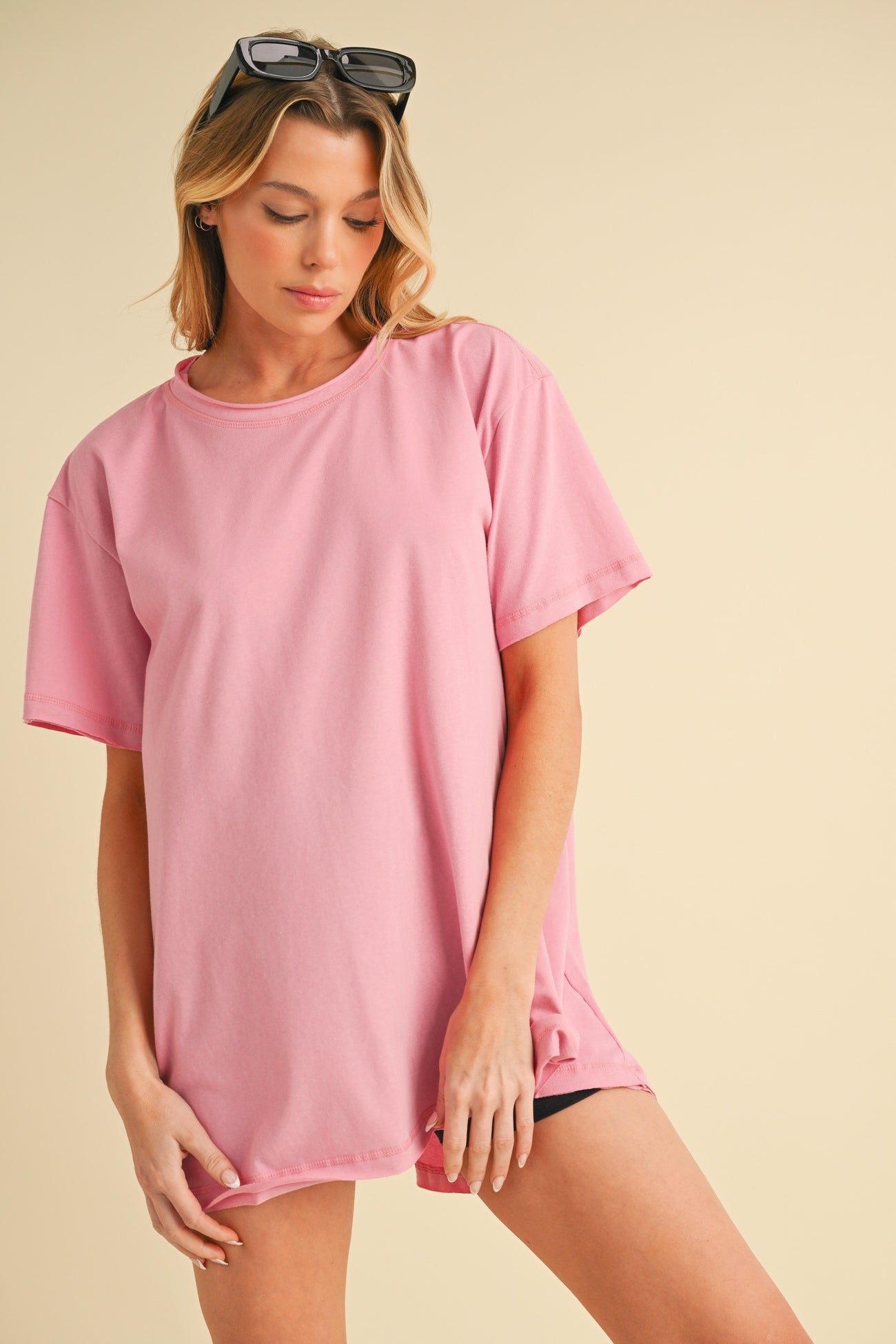 woman wearing an oversized pink t-shirt with rolled sleeves and black shorts, posing against a light background