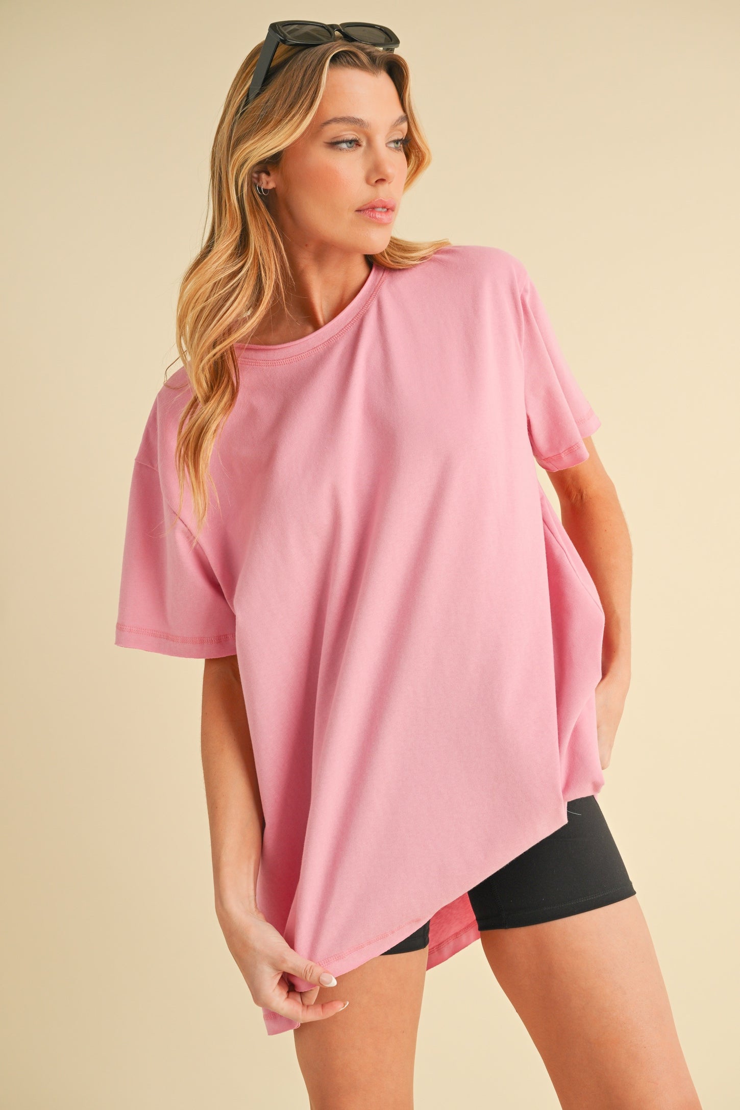 woman wearing a pink oversized t-shirt styled with black biker shorts and sunglasses
