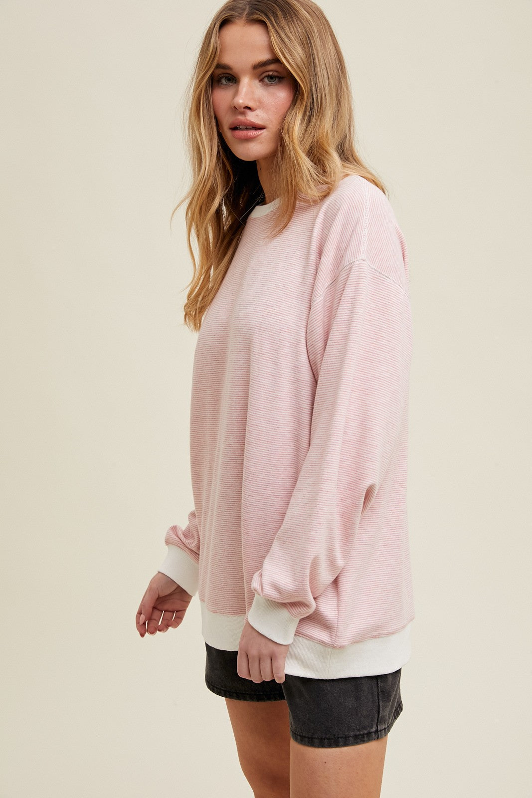 woman wearing a light pink oversized sweatshirt with long sleeves and white cuffs paired with a black mini skirt