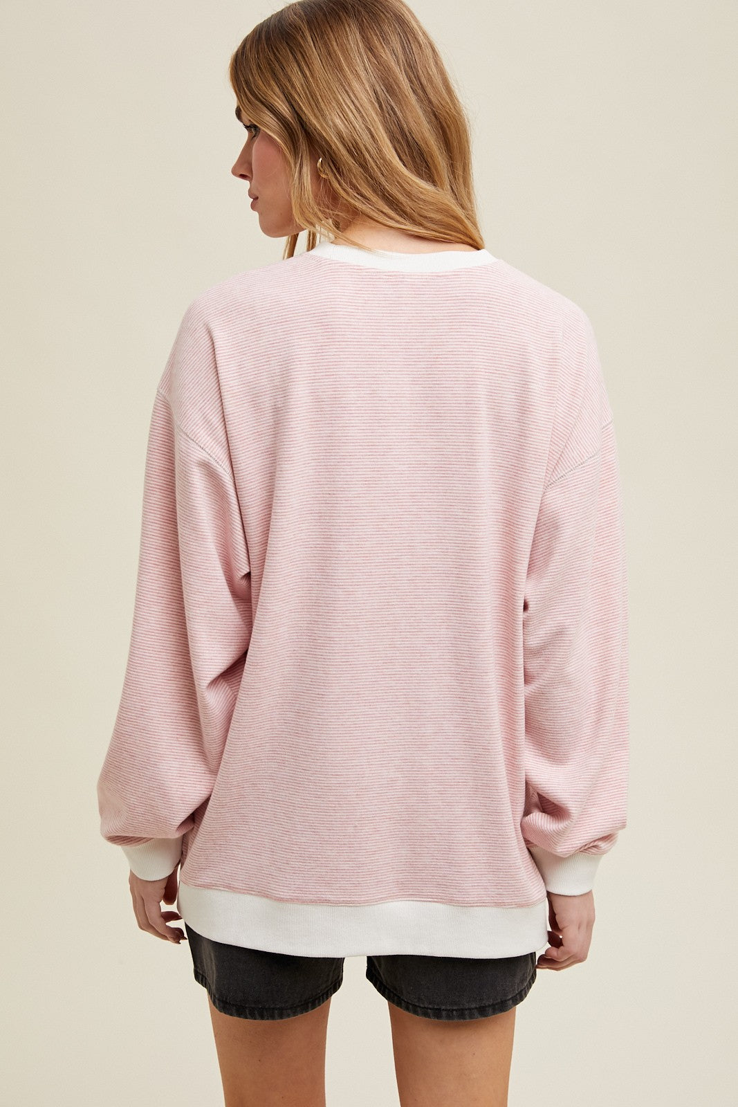 woman wearing a pink oversized sweatshirt with white trim and long sleeves, view from the back