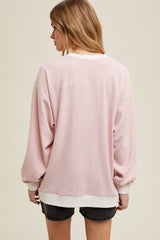 woman wearing a pink oversized sweatshirt with white trim and long sleeves, view from the back