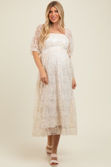 woman wearing a cream lace maternity dress with a square neckline and puff sleeves, showing off her baby bump