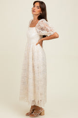 woman wearing a cream floral lace maxi dress with puff sleeves and a square neckline, standing with one hand on her hip