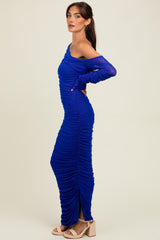 woman wearing a blue one-shoulder ruched maxi dress with long sleeves and a side slit, posing sideways