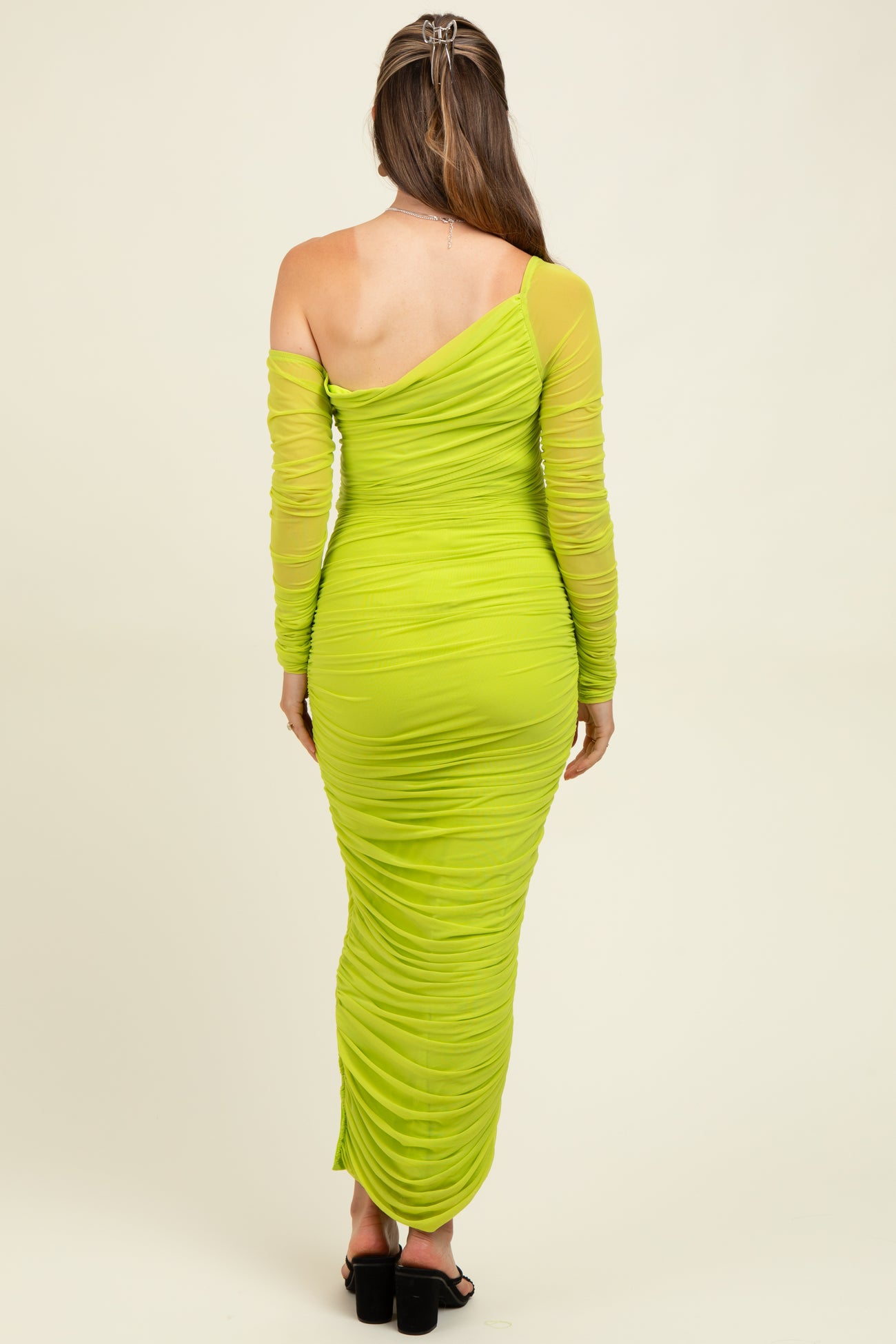 woman wearing a bright green one-shoulder maternity dress with long ruched sleeves, showcasing a fitted silhouette