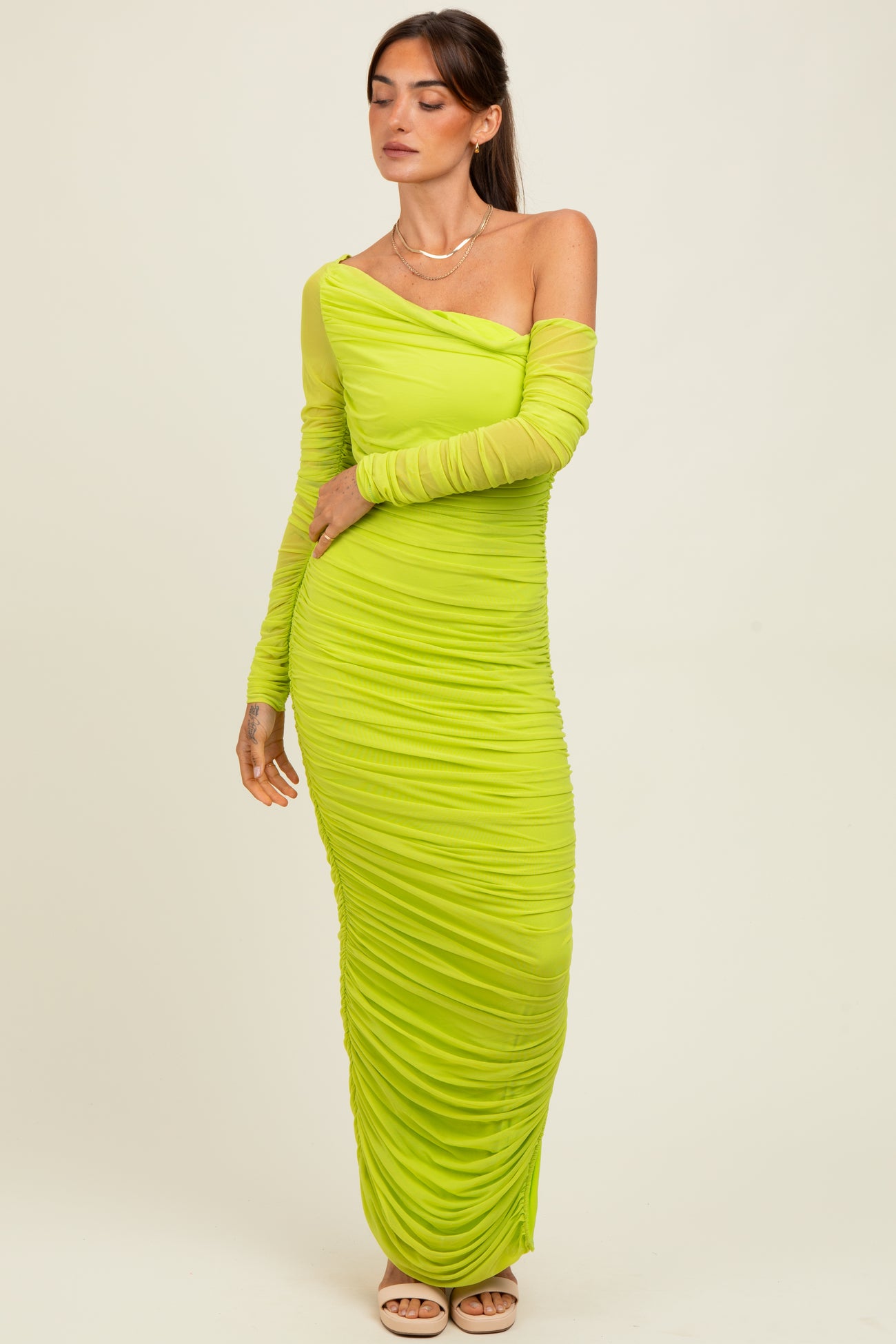woman wearing a one-shoulder bright green ruched maxi dress with long sleeve detail