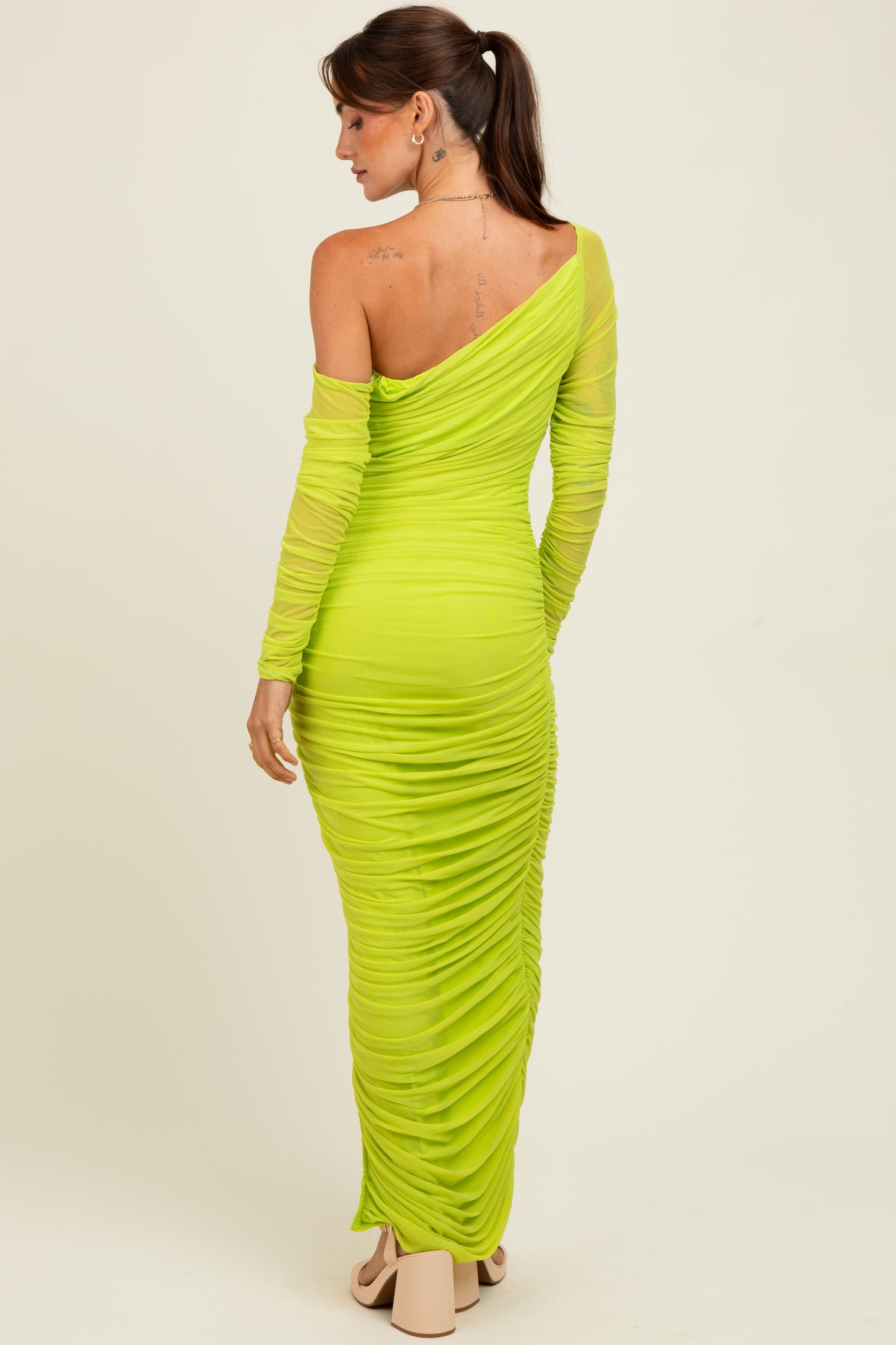 woman wearing a neon green off-shoulder ruched maxi dress with long sleeves and a fitted silhouette