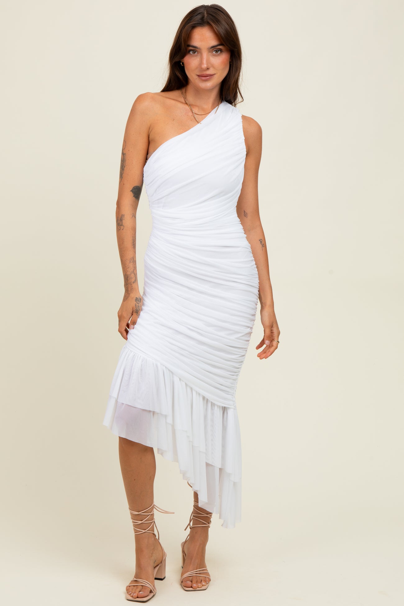 woman wearing a white one-shoulder ruched dress with a layered hem and strappy heels