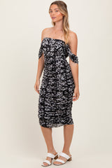 woman wearing a black floral off-the-shoulder midi dress with tie sleeves and ruching details