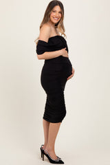 woman wearing a black off-shoulder ruched maternity dress, showcasing her baby bump