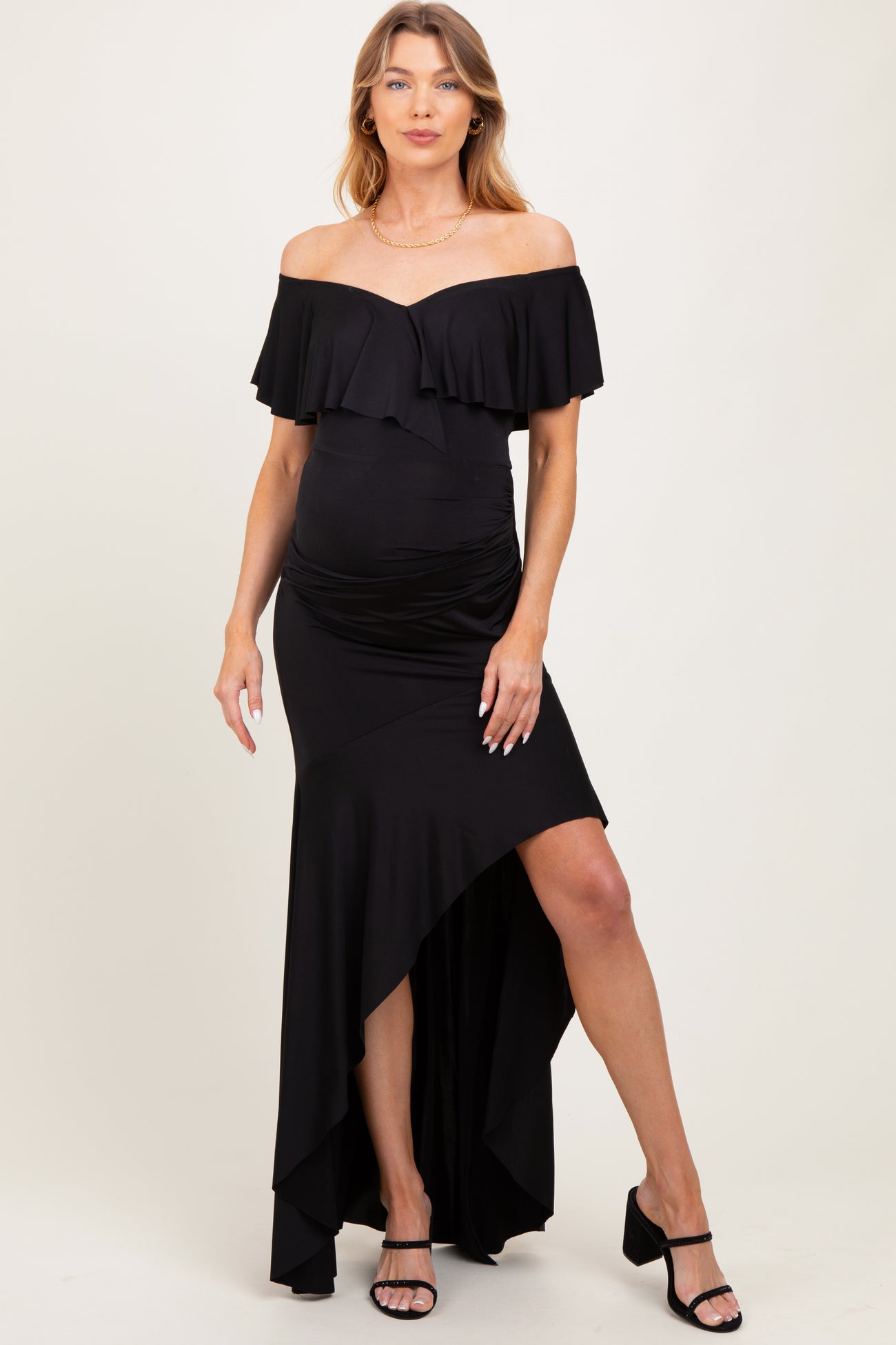 woman wearing a black off-the-shoulder maternity dress with ruffle details and a high-low hem, showcasing her baby bump